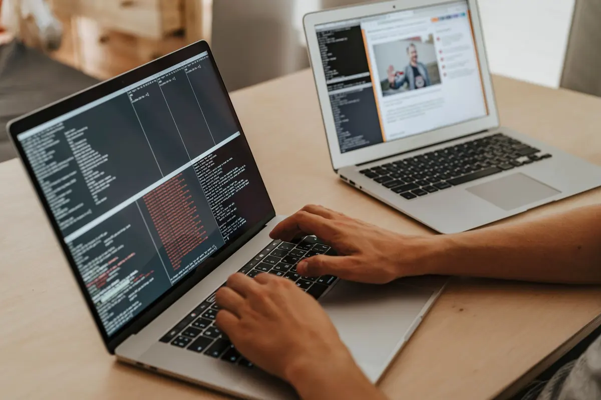A learner typing code on a laptop, with a website open on a second laptop